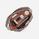 Open beige handbag with various items on a white background