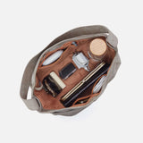 Open beige handbag with various items on a white background