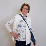 Woman wearing a white jacket with star patterns, holding a blue bag against a plain background