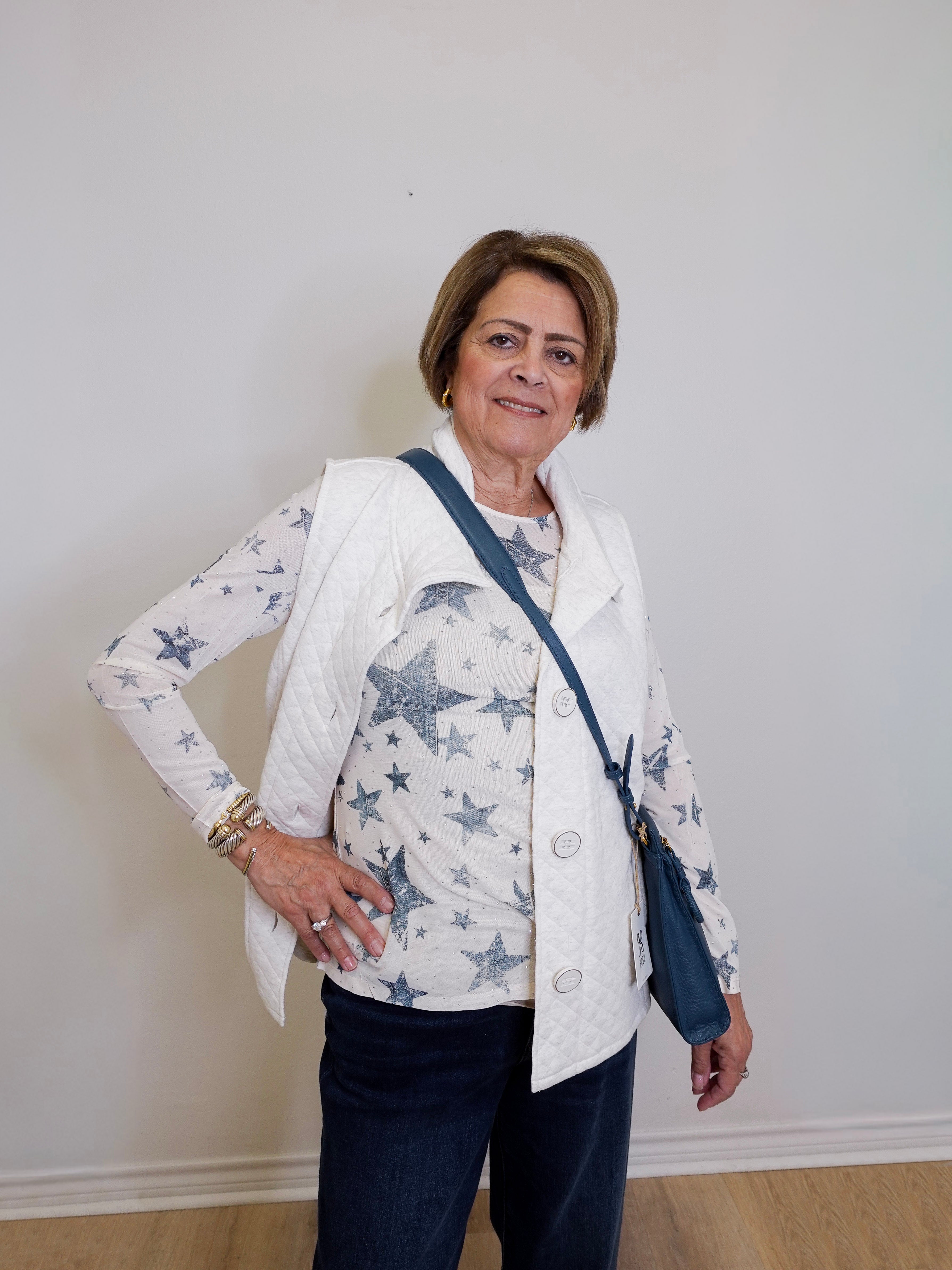 Woman wearing a white jacket with star patterns, holding a blue bag against a plain background
