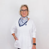 Person wearing a white shirt and black pants with a patterned scarf, standing against a plain background