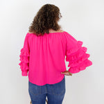 Person wearing a bright pink blouse with ruffled sleeves and blue jeans against a white background
