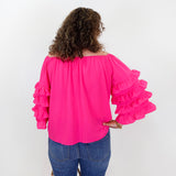 Person wearing a bright pink blouse with ruffled sleeves and blue jeans against a white background