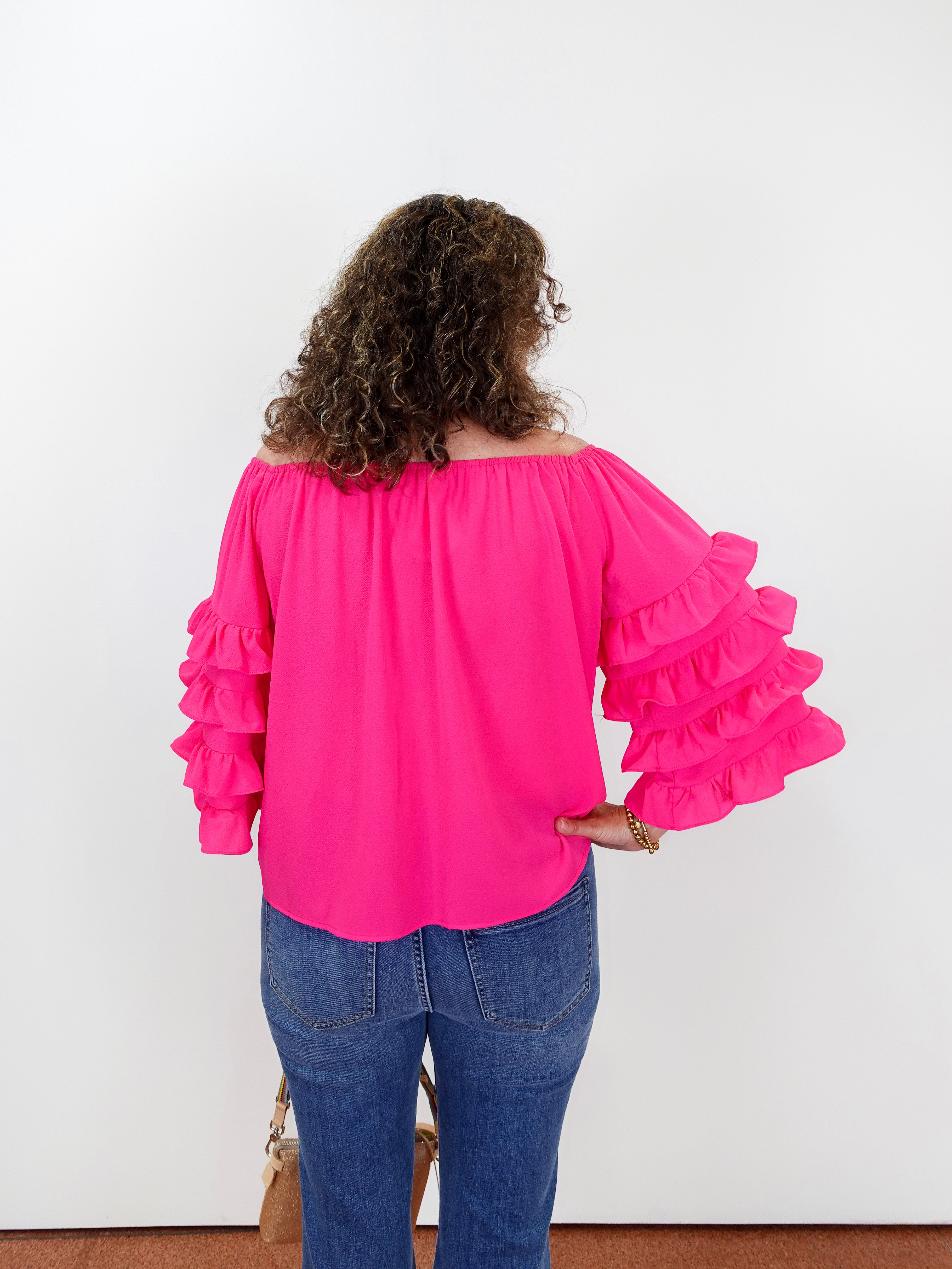 Person wearing a bright pink blouse with ruffled sleeves and blue jeans against a white background