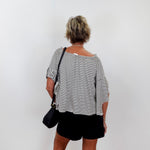 Person wearing a black and white striped shirt and black shorts against a white wall.