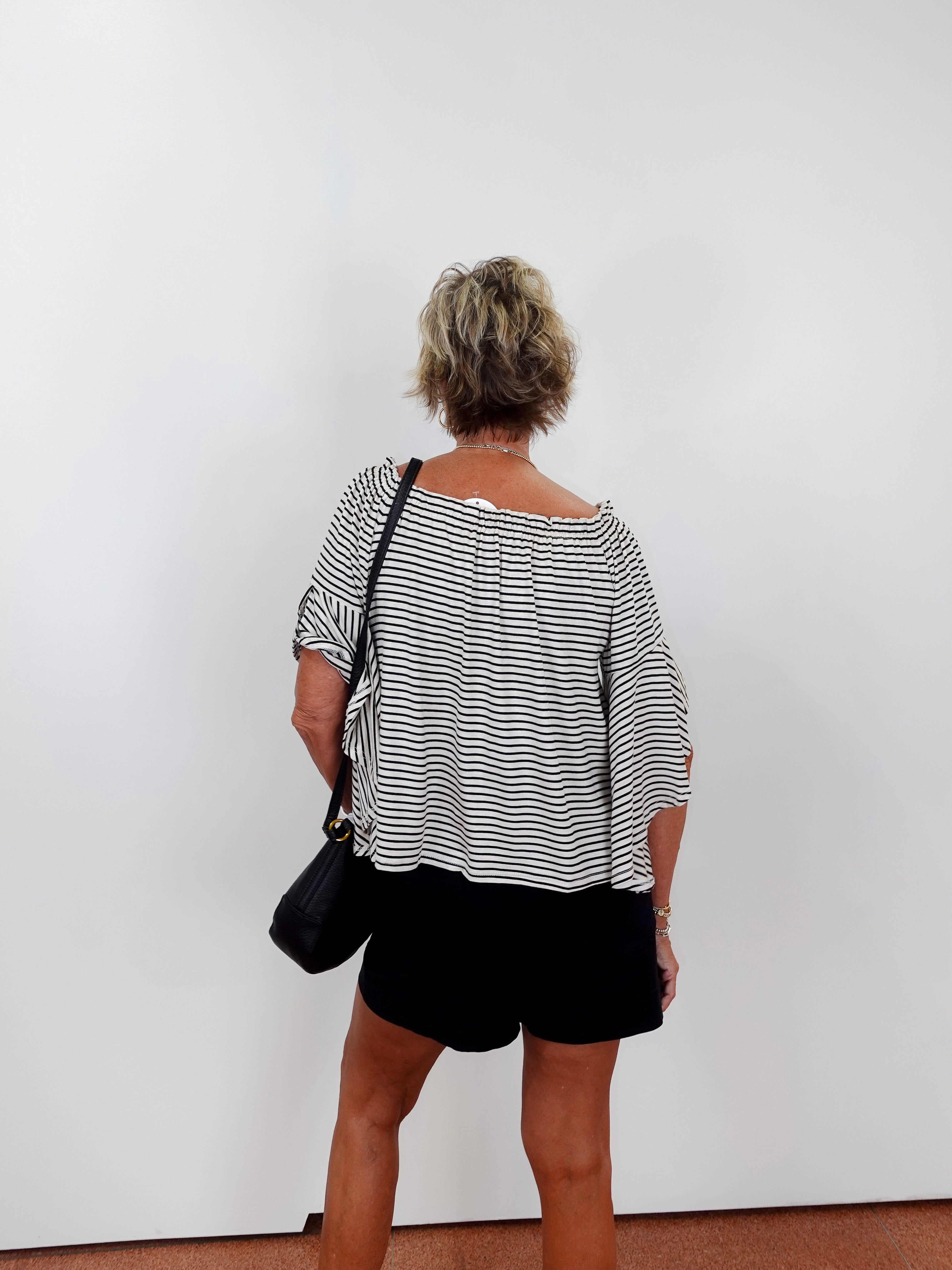 Person wearing a black and white striped shirt and black shorts against a white wall.