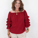 Woman wearing a red blouse with ruffled sleeves and white shorts on a white background