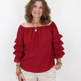Woman wearing a red blouse with ruffled sleeves and white shorts on a white background