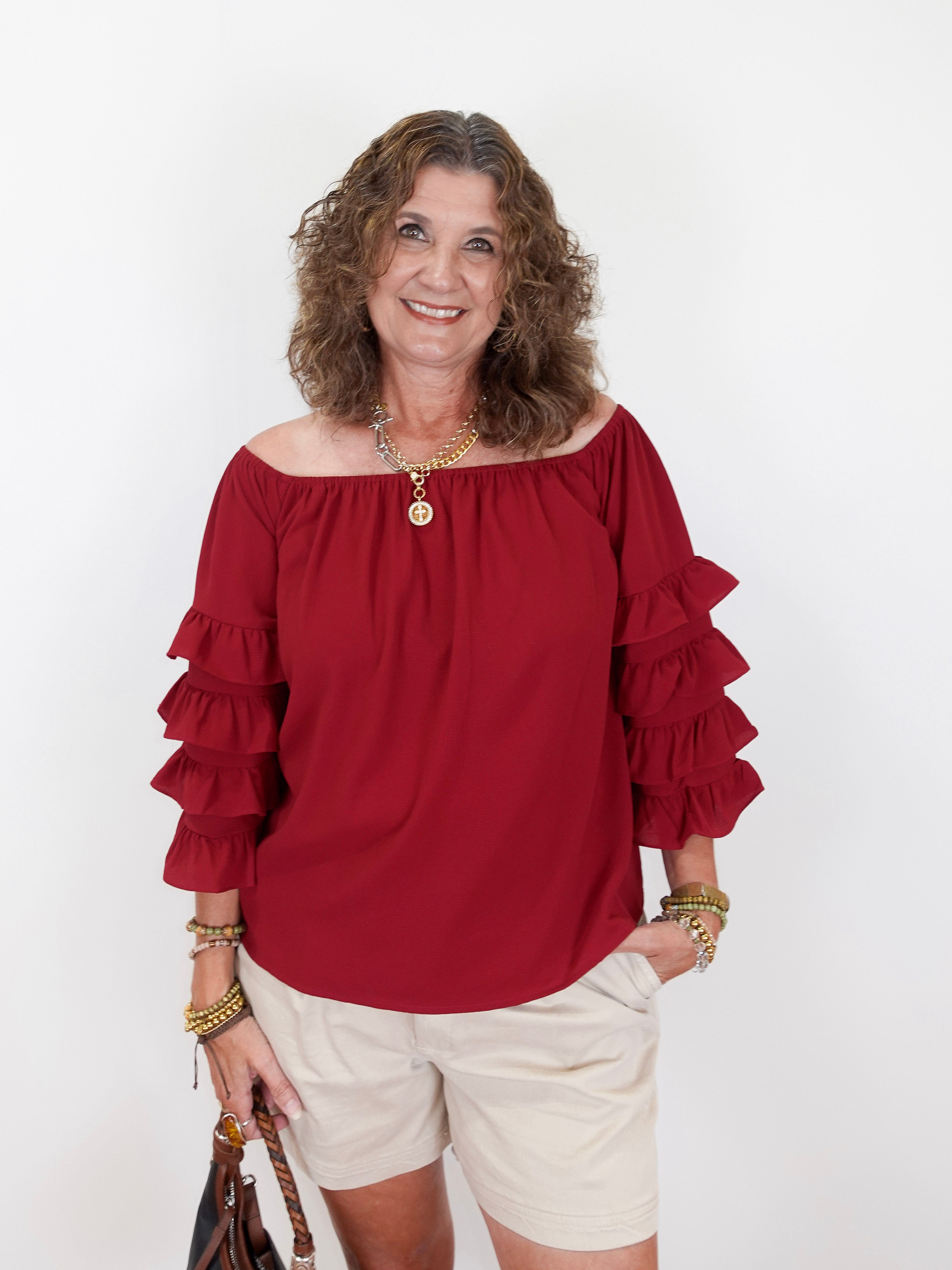Woman wearing a red blouse with ruffled sleeves and white shorts on a white background