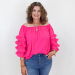Woman wearing a bright pink blouse with ruffled sleeves and blue jeans against a white background
