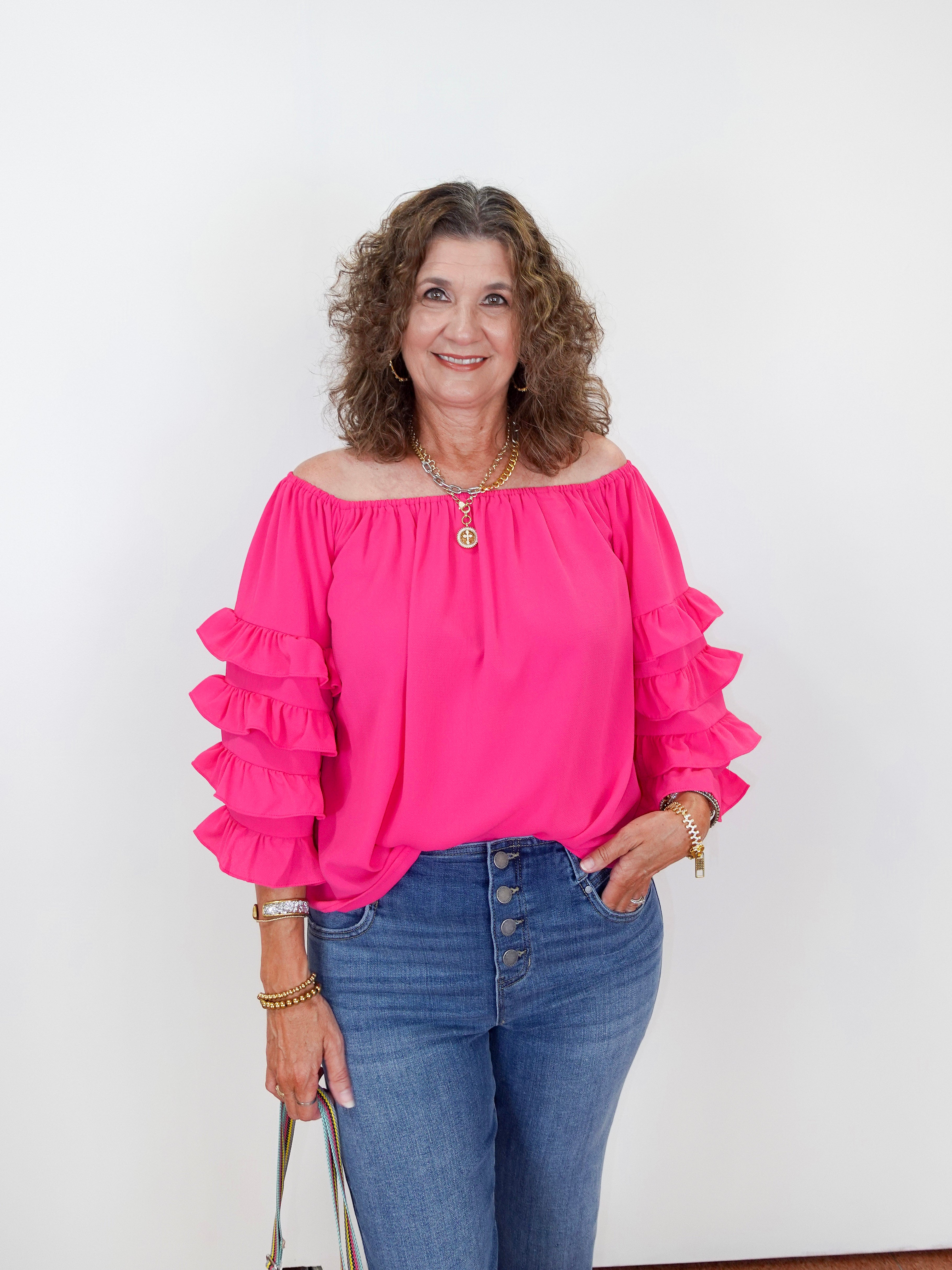 Woman wearing a bright pink blouse with ruffled sleeves and blue jeans against a white background