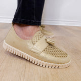 A person modeling a the ilse Jacobsen tassel loafer in gold against a white wall.