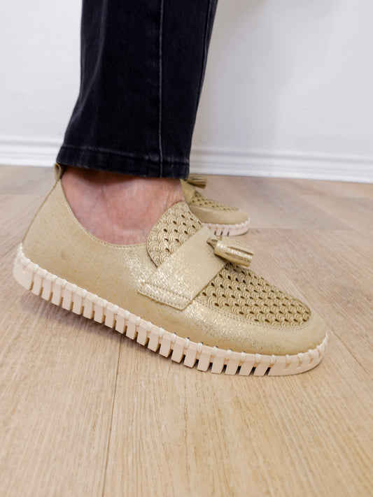 A person modeling a the ilse Jacobsen tassel loafer in gold against a white wall.