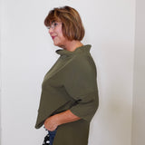 Woman wearing an olive green shirt against a white wall