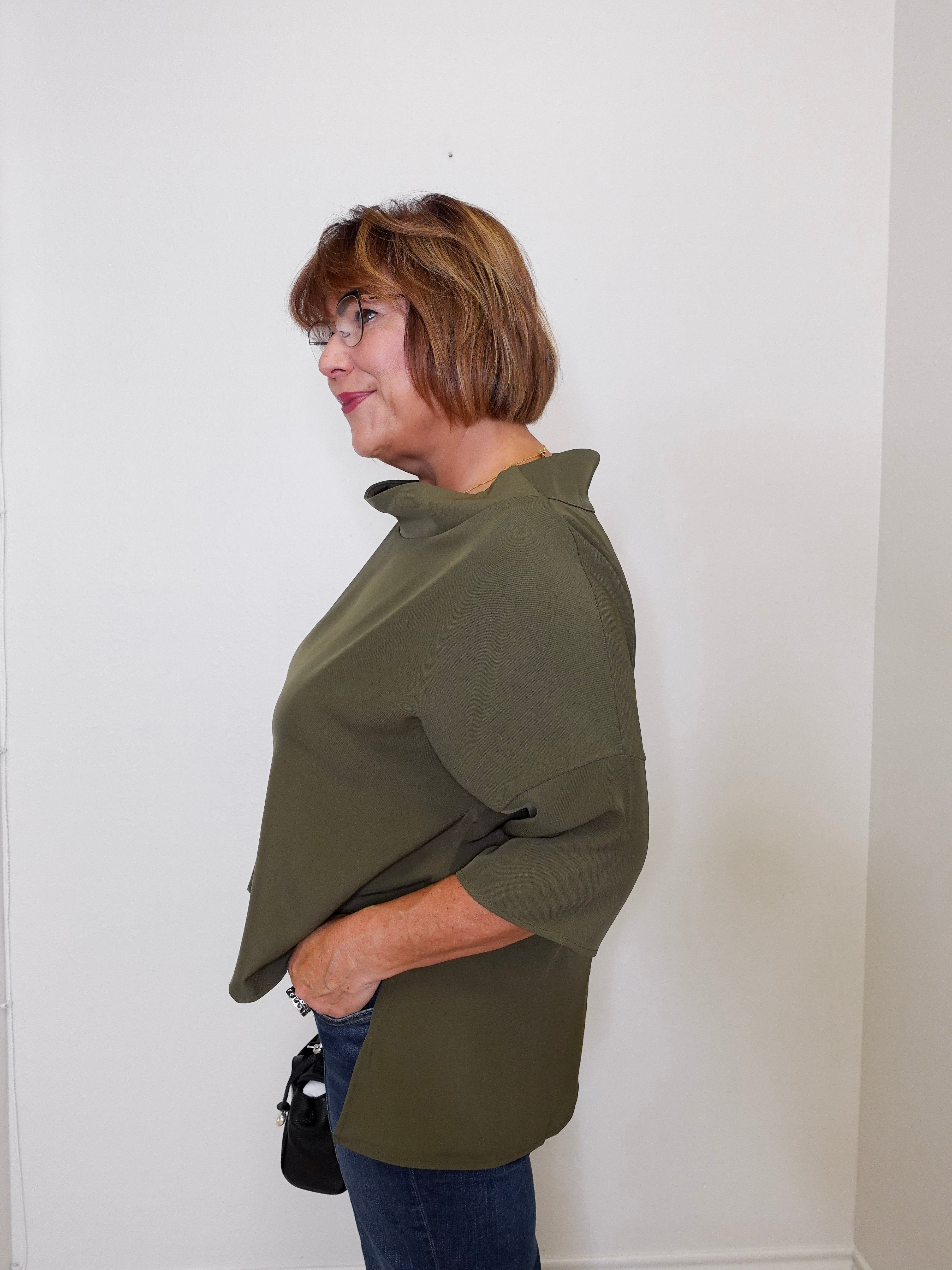 Woman wearing an olive green shirt against a white wall