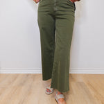 Person wearing green olive green pants and a black top with floral embroidery on a white background