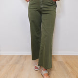 Person wearing green olive green pants and a black top with floral embroidery on a white background