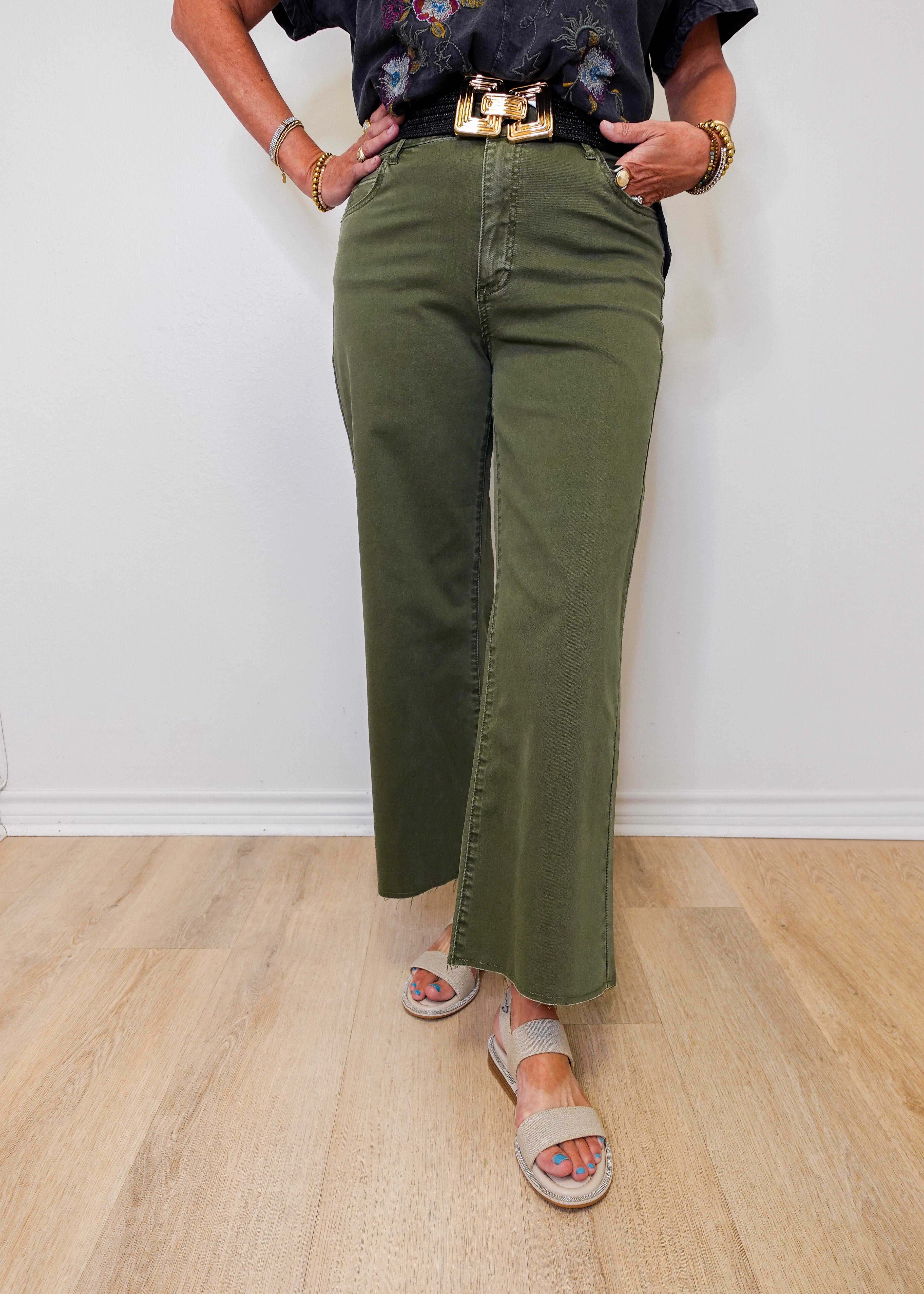 Person wearing green olive green pants and a black top with floral embroidery on a white background