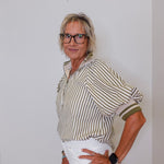 Woman wearing a striped shirt and white pants against a plain background