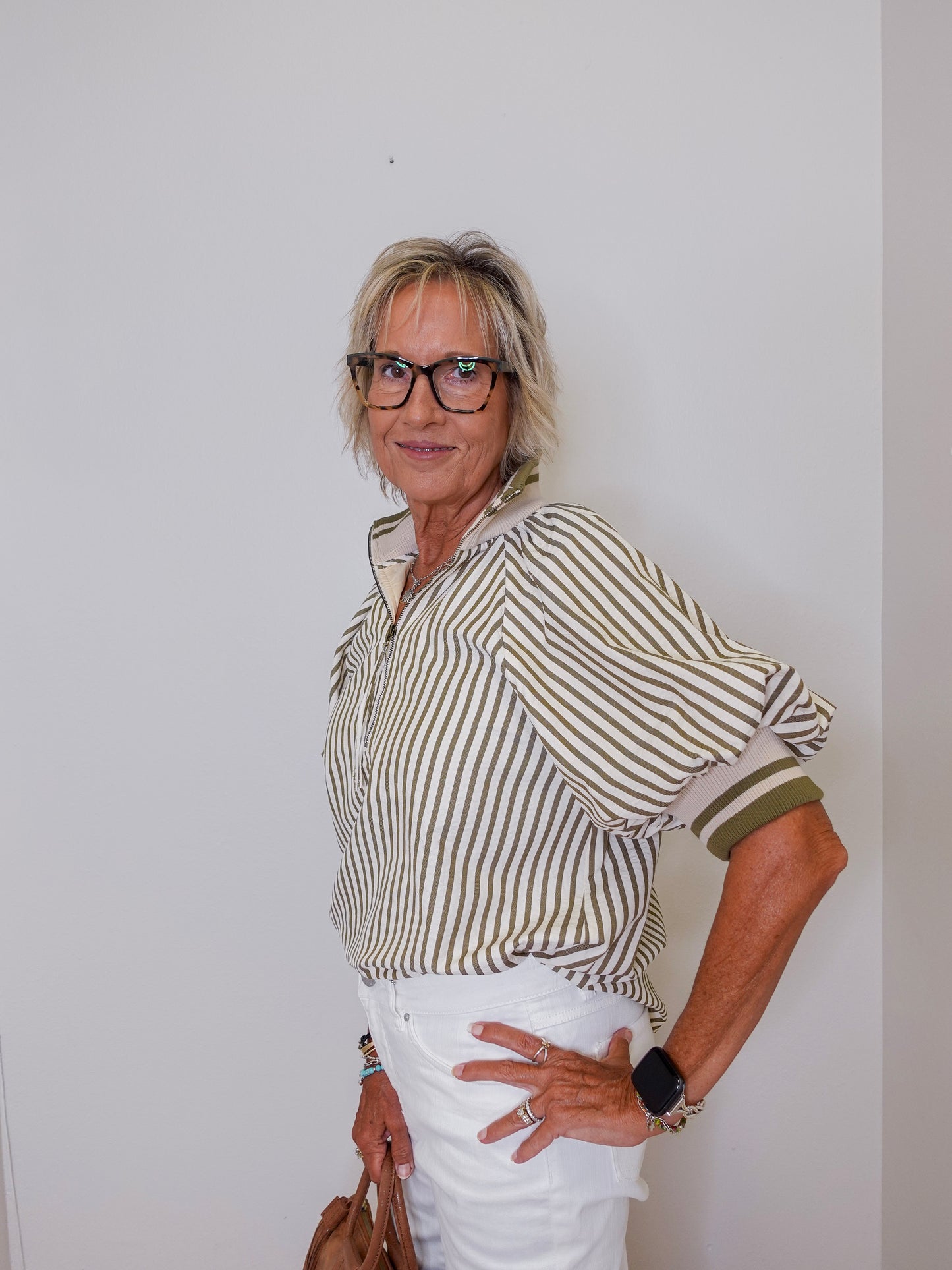Woman wearing a striped shirt and white pants against a plain background