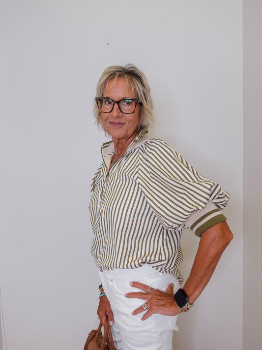 Woman wearing a striped shirt and white pants against a plain background