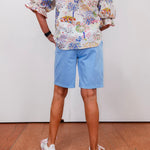 Person wearing a floral shirt and light blue shorts standing on a wooden floor.