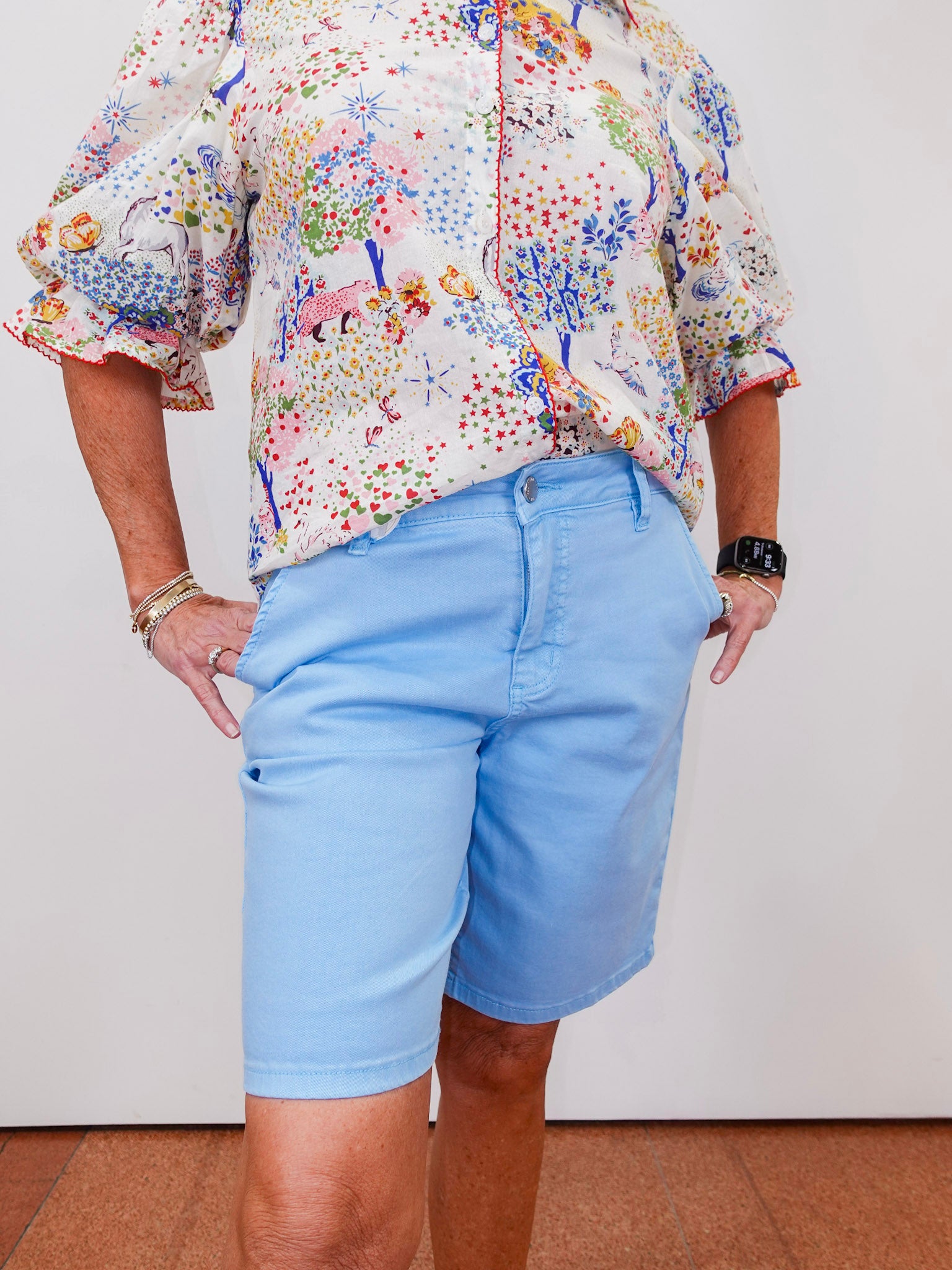 Person wearing a colorful floral blouse and light blue shorts on a plain background