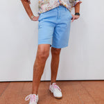 Person wearing a floral shirt, light blue shorts, and white sneakers on a plain background
