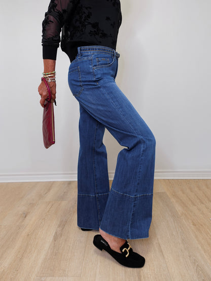 A woman modeling French dressing jeans the olivia bootleg jean against a white wall. 