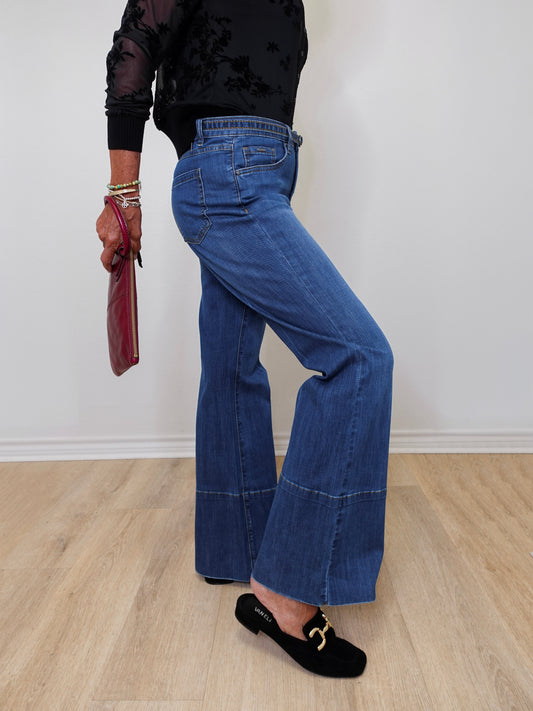 A woman modeling French dressing jeans the olivia bootleg jean against a white wall. 