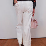 Person wearing white pants and a floral sweater, holding a pink handbag against a plain background