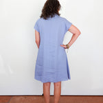 Person wearing a light blue dress standing against a white wall.
