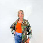 Woman wearing a camouflage jacket over an orange shirt with blue jeans on a white background