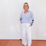 Person wearing a striped shirt and white pants standing against a white wall.