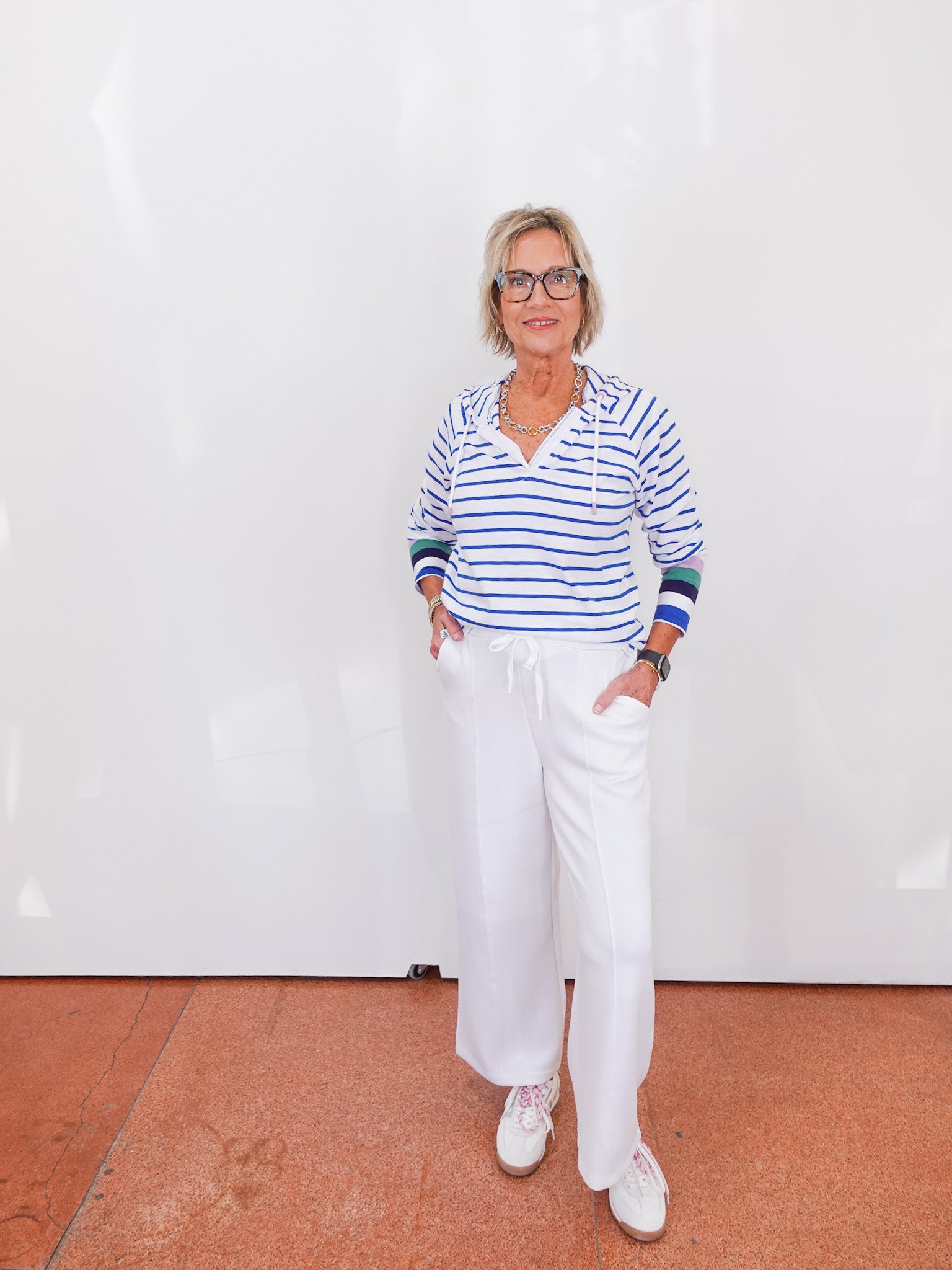 Person wearing a striped shirt and white pants standing against a white wall.
