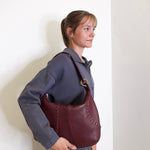 Woman holding a maroon leather handbag against a white background