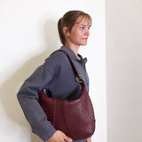Woman holding a maroon leather handbag against a white background