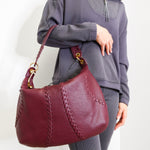 Person holding a maroon handbag against a white background