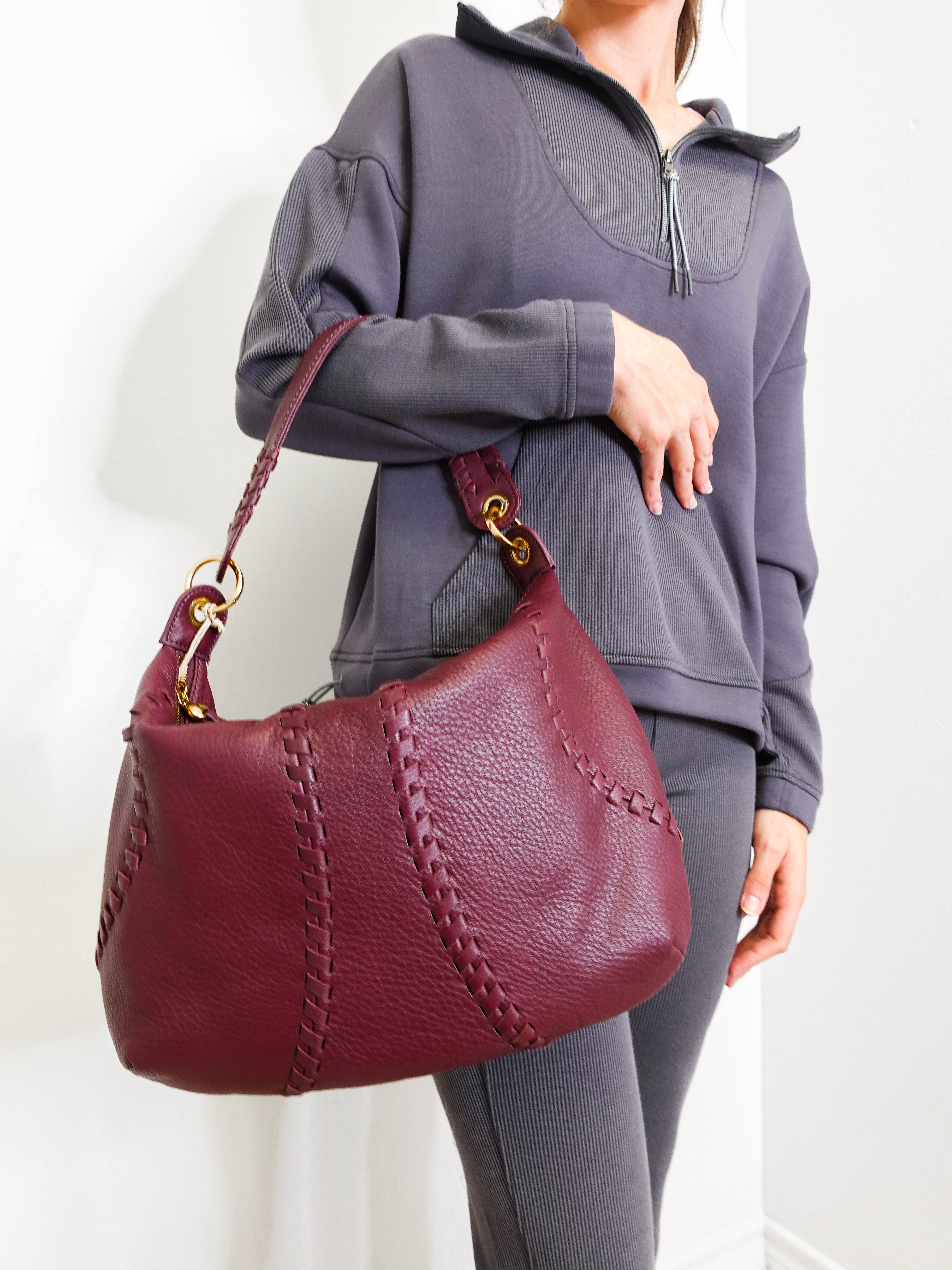 Person holding a maroon handbag against a white background