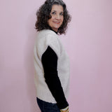 Woman wearing a white sweater with black sleeves against a pink wall