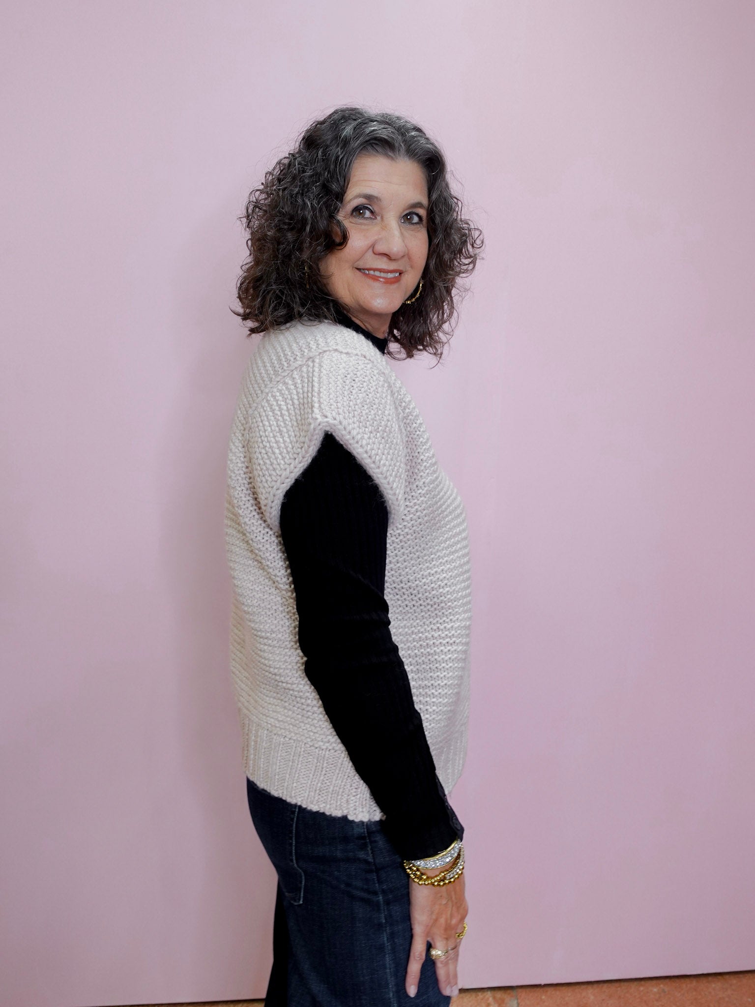 Woman wearing a white sweater with black sleeves against a pink wall