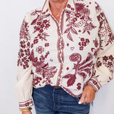 Woman wearing a floral patterned blouse with red designs on a white background