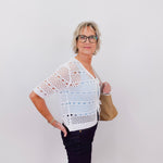 Woman wearing a white crochet top and black pants against a plain background
