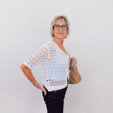 Woman wearing a white crochet top and black pants against a plain background