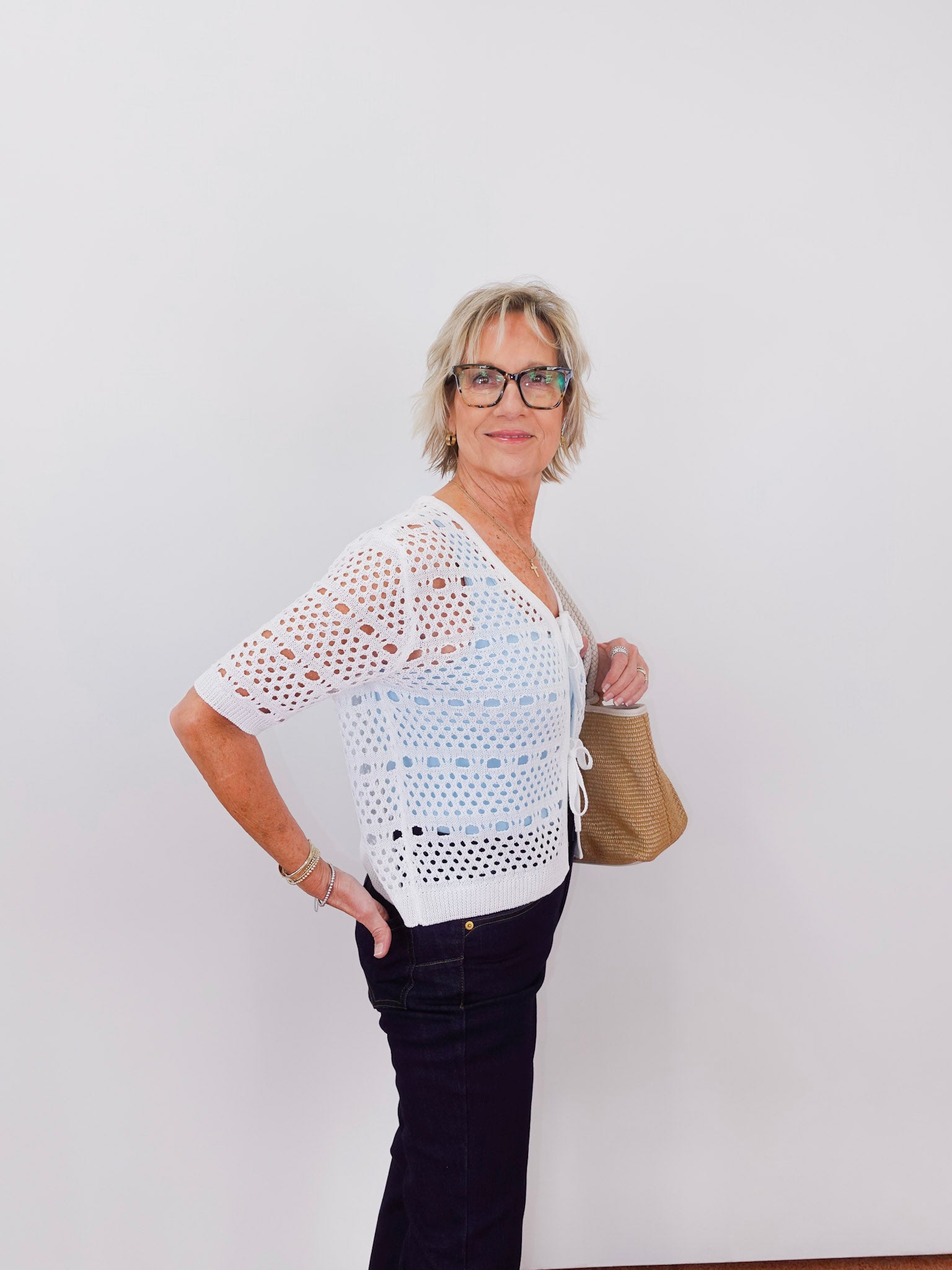 Woman wearing a white crochet top and black pants against a plain background
