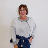 Woman wearing a light gray sweater with a denim belt against a white background