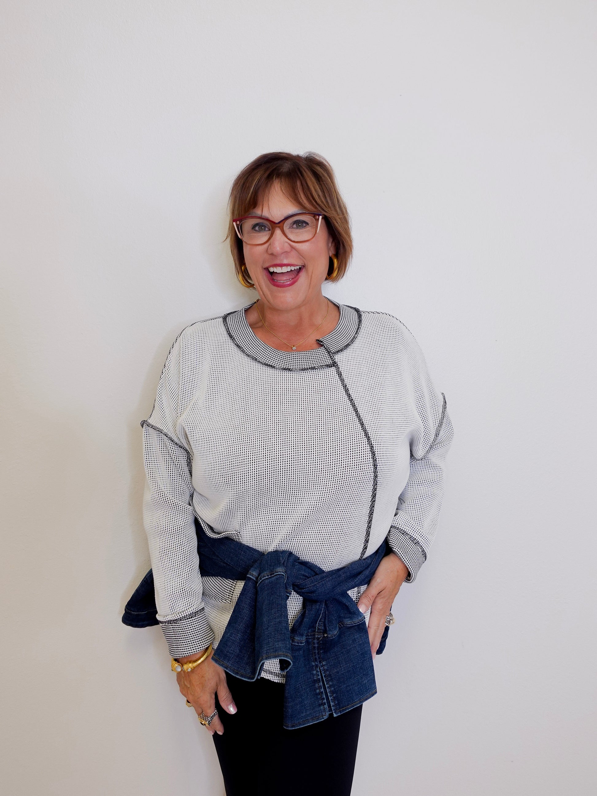 Woman wearing a light gray sweater with a denim belt against a white background