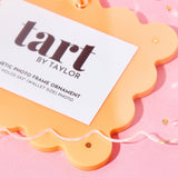 Orange photo frame ornament with a label on a pink background