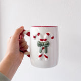 Hand holding a mug with a candy cane design against a white background