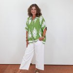 Woman wearing a green patterned shirt and white pants against a plain background